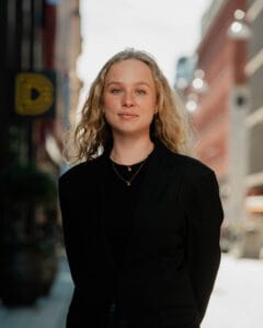 Kvinna i svart tröja står på stadsgata med affärer och belysning i bakgrunden