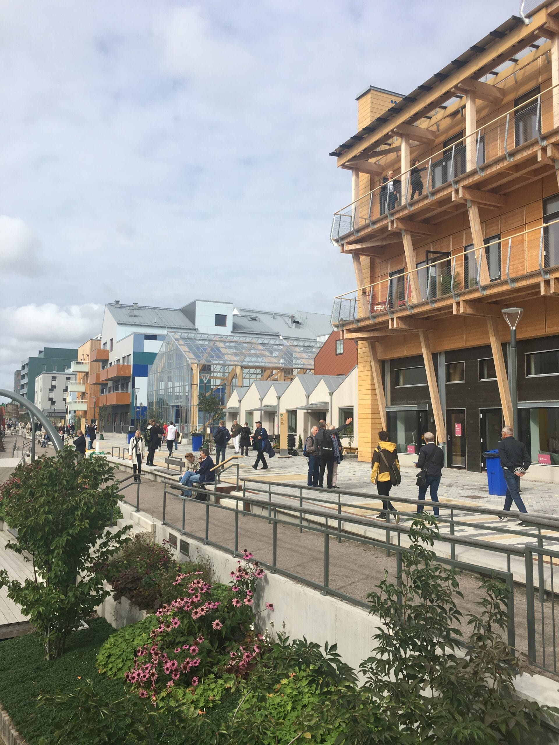 Centrumtorg med bostadslägenheter, kommersiella lokaler och gågata där personer rör sig mellan byggnaderna