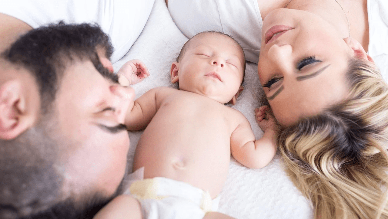 Föräldrar med nyfödd baby ligger tillsammans i säng