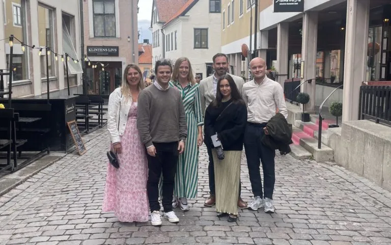 Sex personer står tillsammans på kullerstensgata i historisk stadsmiljö med affärer och restauranger